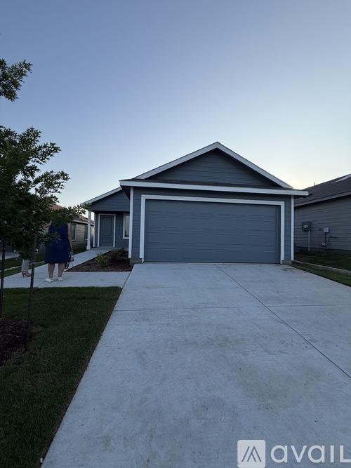A woman in a blue dress is walking towards a house with a grey garage door.