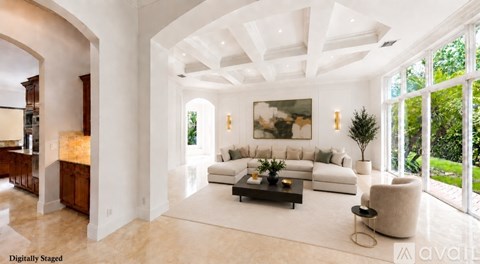 A spacious living room with a large painting on the wall and a view of the garden outside.