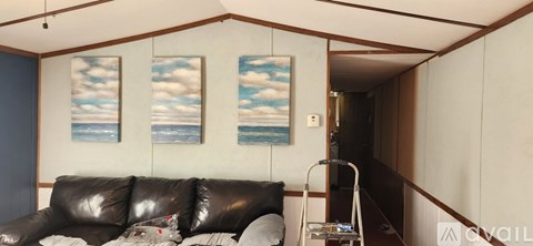 A living room with a black leather couch and two paintings on the wall.
