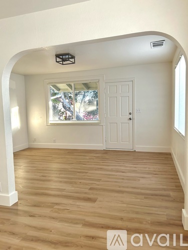 A room with wooden flooring and a window showing trees outside.