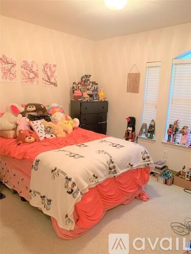 A bedroom with a bed covered in a white and pink comforter and a black dresser with stuffed animals on top.
