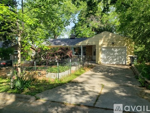 A house with a garage is surrounded by greenery and has a driveway leading to the garage.