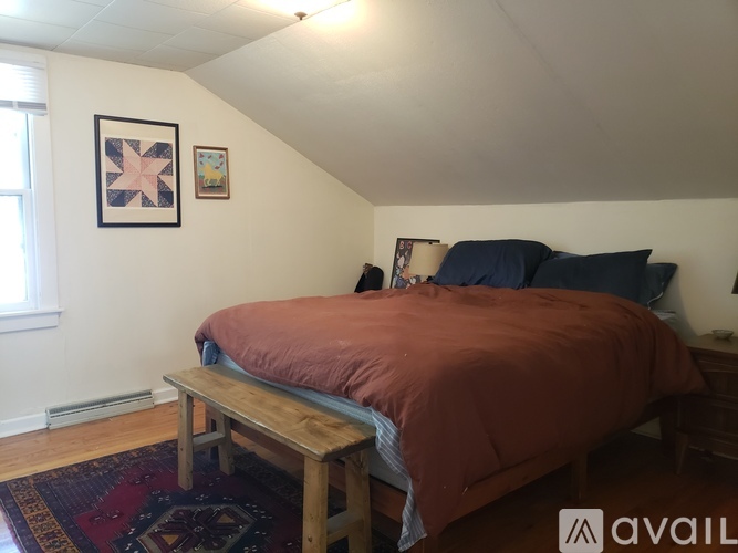A bedroom with a bed, bench, and two pictures on the wall.