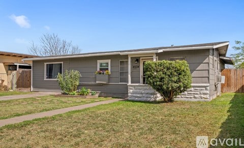 A house with a grey exterior and a front yard with a bush and a tree.