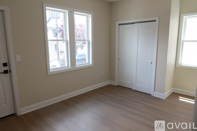 A room with a white door, a window with a view of a tree and a building outside, and a white wardrobe.