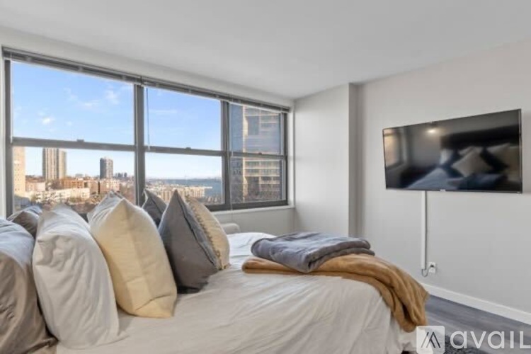 A bedroom with a large bed and a city view through the window.