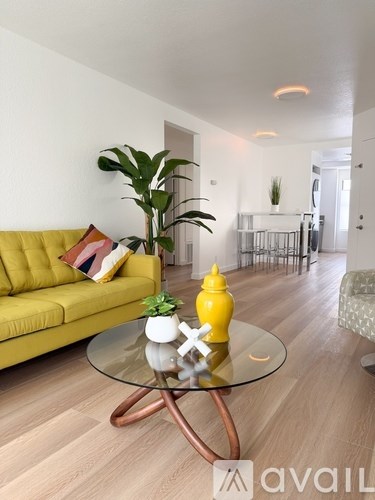 A living room with a yellow couch and a glass coffee table.