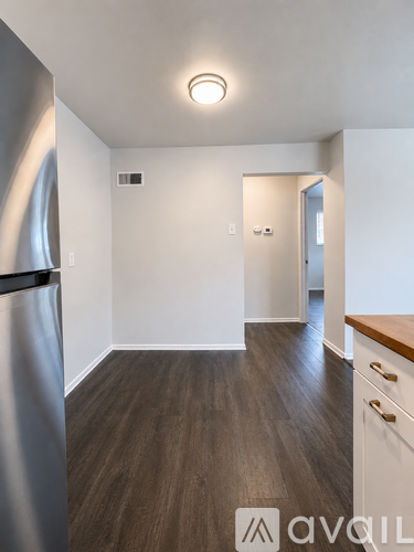 A kitchen with a refrigerator, wooden floors, and white walls.