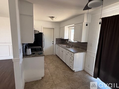 A kitchen with white cabinets and a black refrigerator.