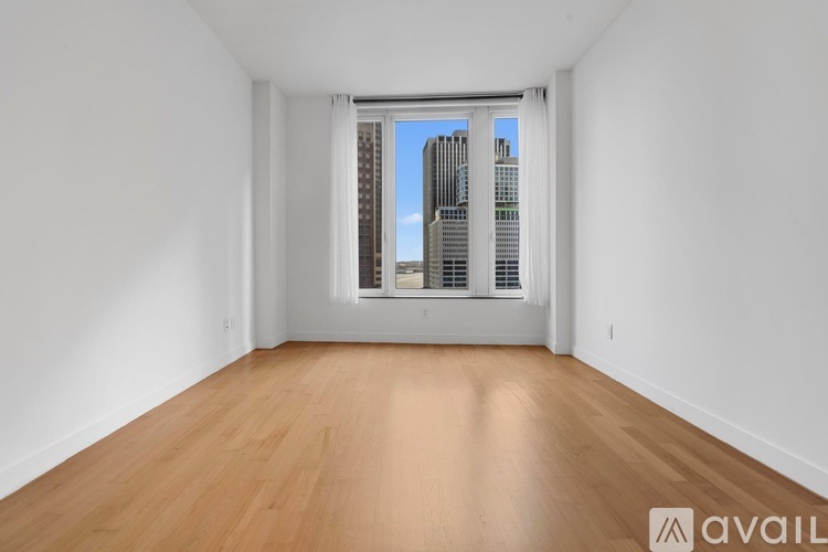 A large empty room with wooden floors and a window overlooking a city skyline.