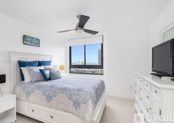 A bedroom with a bed, a television, and a window with a view of a city.