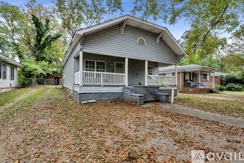 A house with a porch and a covered patio is surrounded by trees and leaves on the ground.