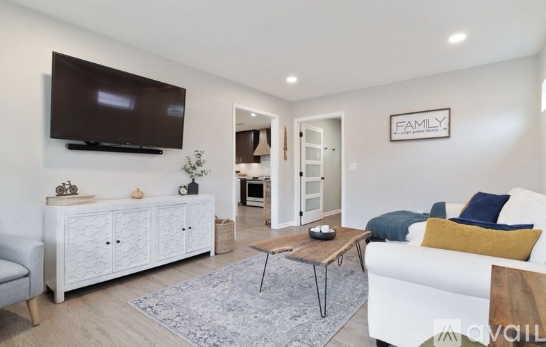 A living room with a white couch, a wooden coffee table, and a flat-screen TV mounted on the wall.