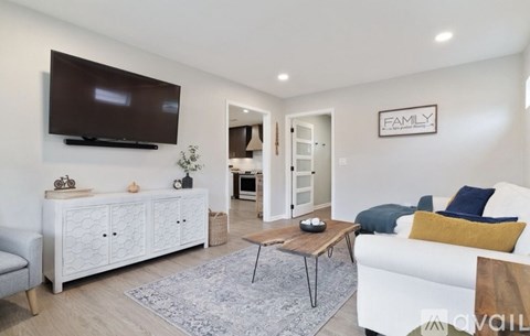 A living room with a white couch, a wooden coffee table, and a flat-screen TV mounted on the wall.