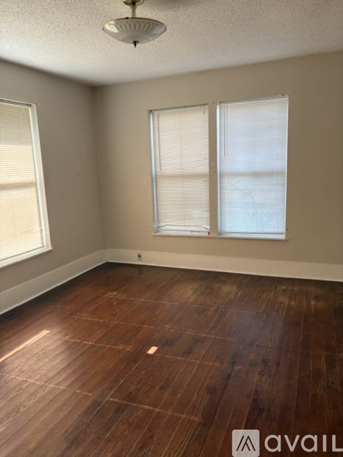 A room with wooden flooring and two windows.