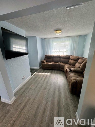 A living room with a brown couch and a flat screen TV mounted on the wall.