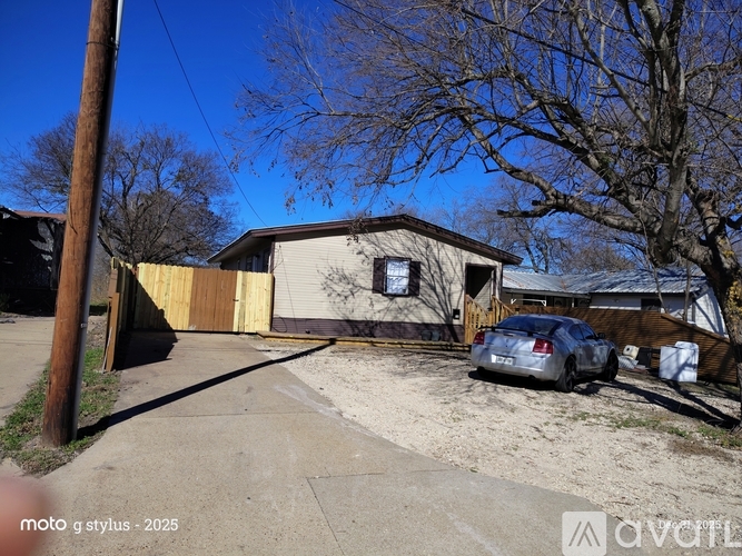 A car is parked in front of a house with a brown fence.