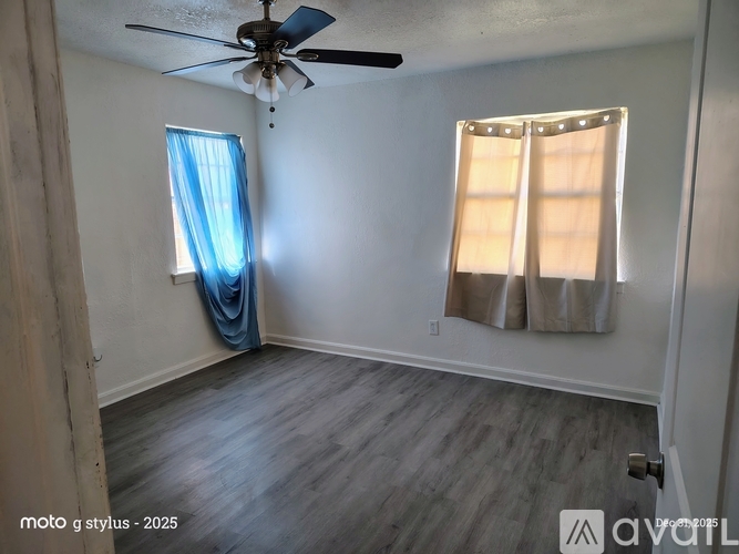 A room with a ceiling fan and two windows with curtains.