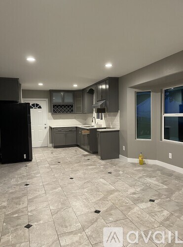 A kitchen with a black refrigerator and grey cabinets.