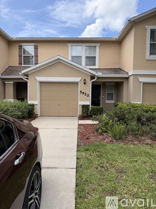A brown car is parked in front of a beige house with a garage.