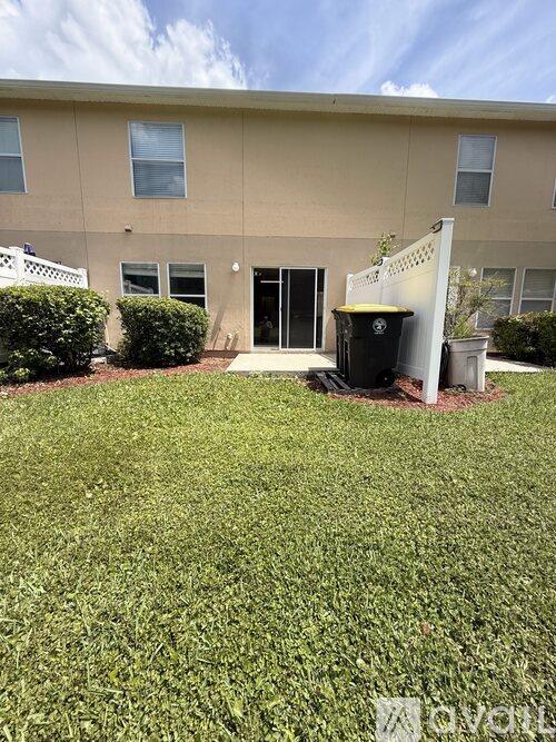 A beige building with a white fence and a black trash can in front.