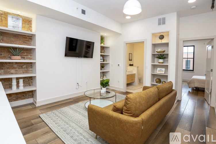 A living room with a brown couch, a glass table, and a flat-screen TV mounted on the wall.