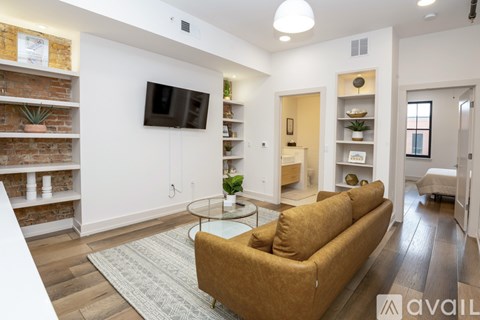 A living room with a brown couch, a glass table, and a flat-screen TV mounted on the wall.