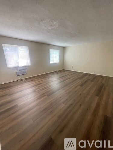 A room with wooden flooring and two windows.
