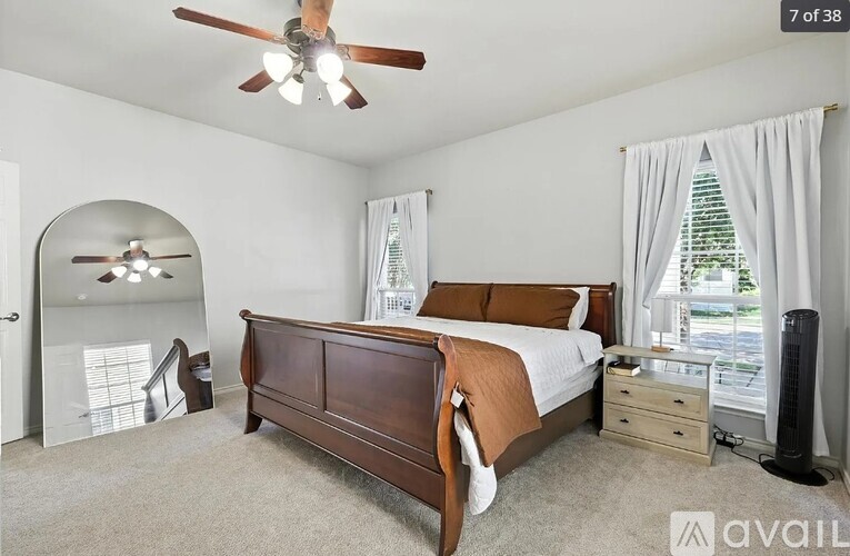 A bedroom with a large bed, a ceiling fan, and a window with white curtains.