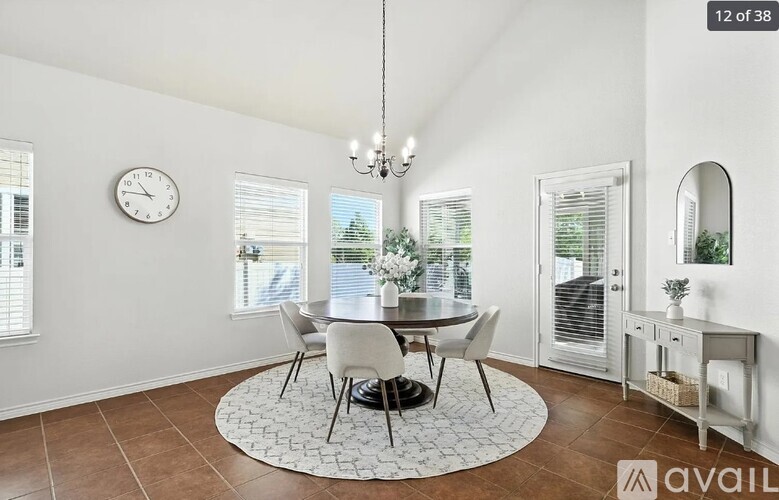A dining room with a round table and chairs, a chandelier, and a clock on the wall.