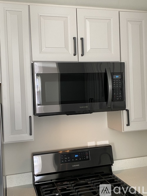 A black microwave is mounted above a black stove.