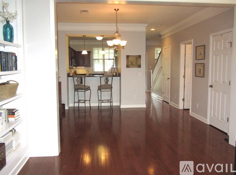 A living room with a kitchen in the background and a dining table with chairs in the foreground.