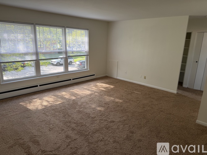 A room with a carpeted floor and a large window with blinds.