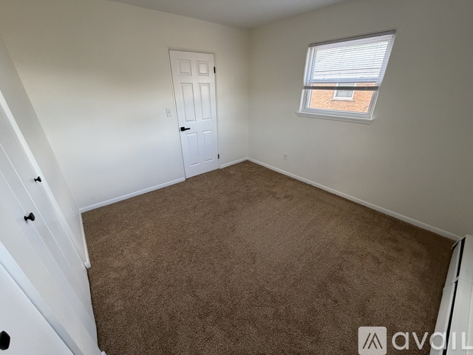 A room with a carpeted floor, a door, and a window with a view of a brick building outside.