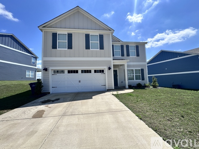 A two-story house with a garage is surrounded by a well-maintained lawn and other houses.