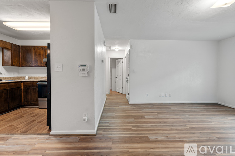 A spacious room with wooden flooring and white walls, leading to a hallway.