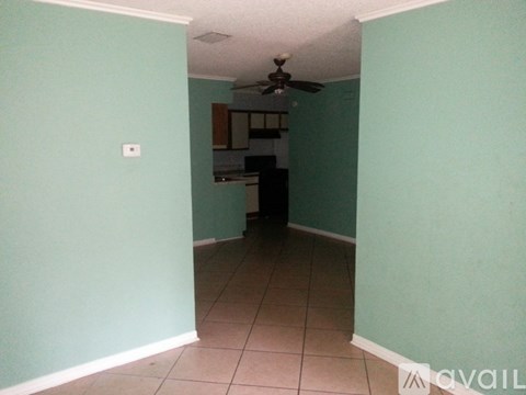 A room with a ceiling fan and a kitchen in the background.