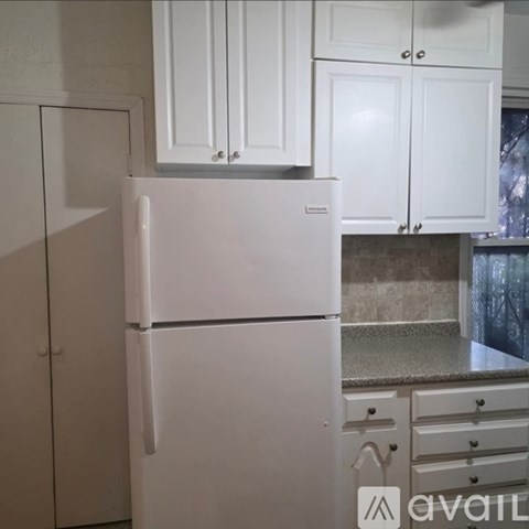 A white refrigerator in a kitchen with white cabinets.