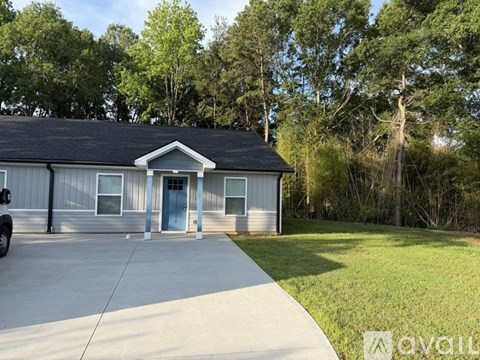 A house with a grey roof and a blue door is surrounded by greenery.