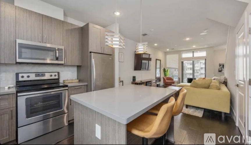 A modern kitchen with a stainless steel oven and microwave, a white island, and a dining area with a bench.
