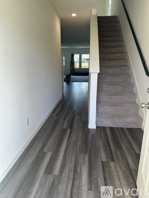 A hallway with a staircase and wooden flooring.