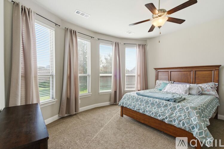 A bedroom with a bed, a ceiling fan, and a window with curtains.