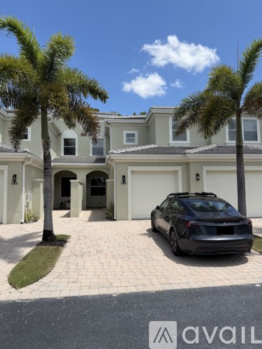 A black car is parked in front of a house with a palm tree.