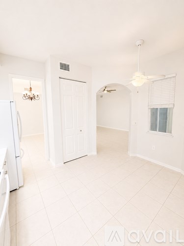 A white kitchen with a fridge and a fan.