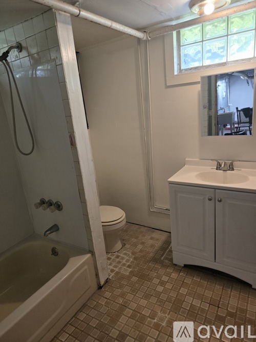 A bathroom with a white tub and toilet, a sink with a mirror above it, and a window.