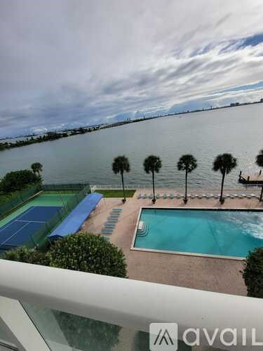A pool and tennis court with palm trees and a bridge in the background.