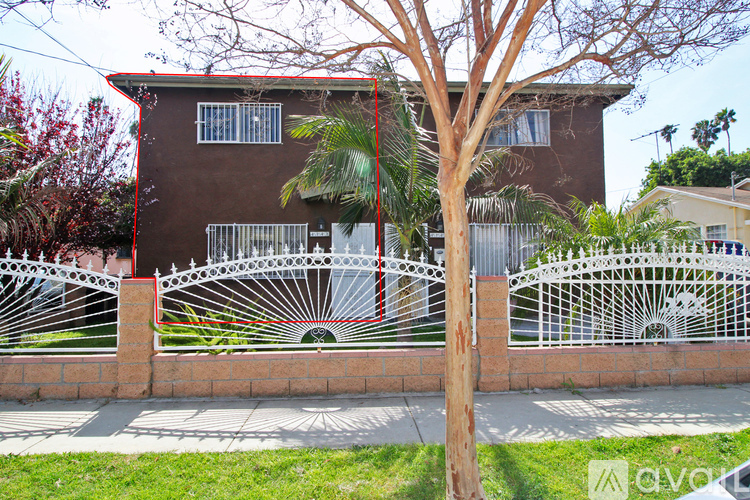 A brown house with a white fence and a tree in front.