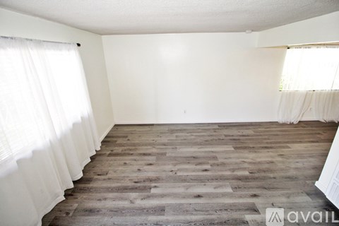A room with wooden flooring and white curtains.