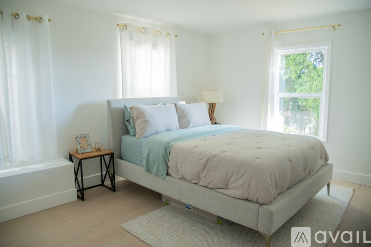 A bedroom with a large bed and a window with white curtains.