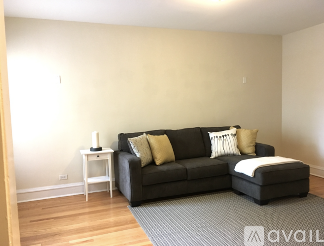 A black couch with a white pillow and a small white table with a lamp on it.